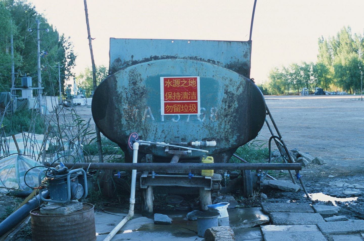 Rusted teal water tank with pipes and Chinese sign.